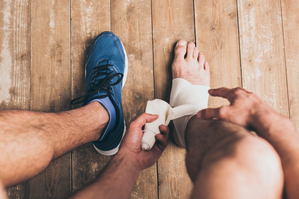 vista recortada del deportista en una zapatilla de deporte vendaje pierna lesionada con vendaje elástico
 - Foto, imagen