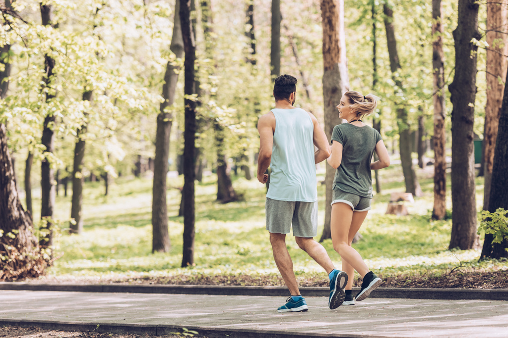 jeune homme en femme en vêtements de sport parler tout en faisant du jogging dans le parc vert
 - Photo, image