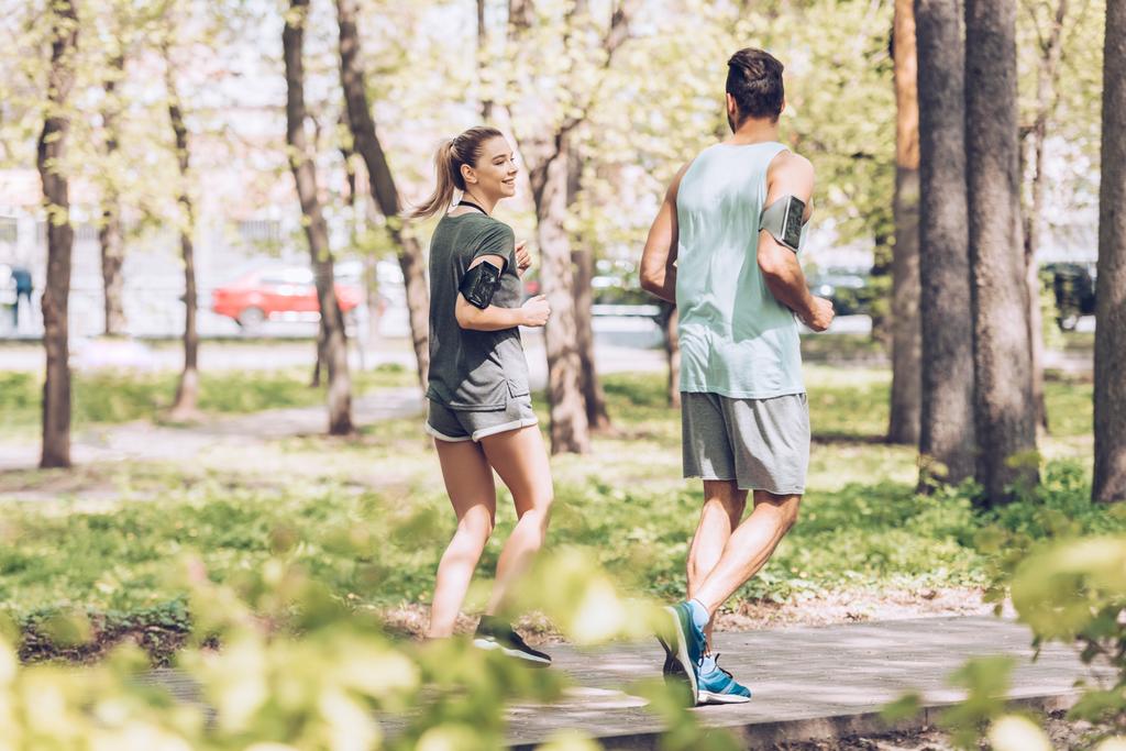 Молодой человек и женщина разговаривают во время пробежки вместе в солнечном парке
 - Фото, изображение