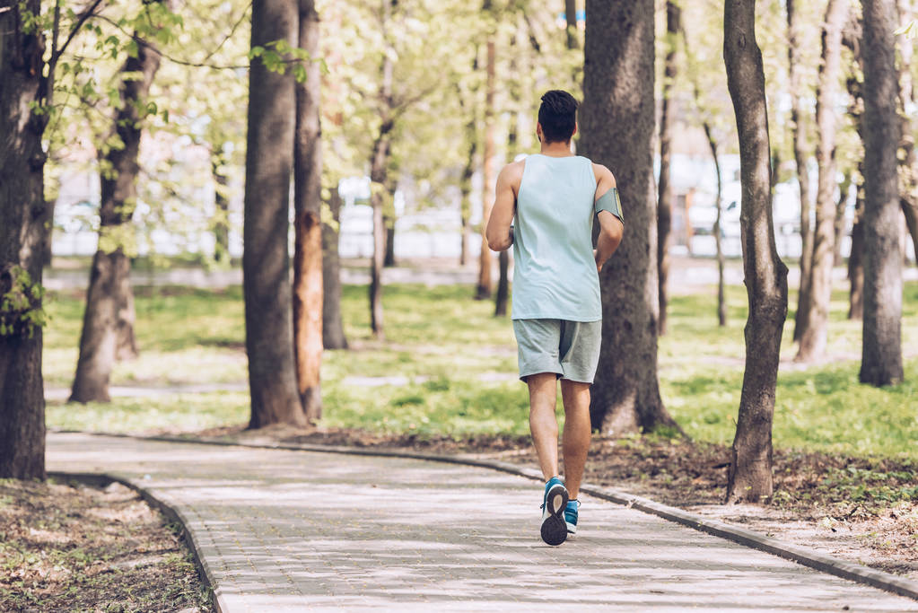 Rückansicht junger Sportler joggt auf Gehweg im Park - Foto, Bild