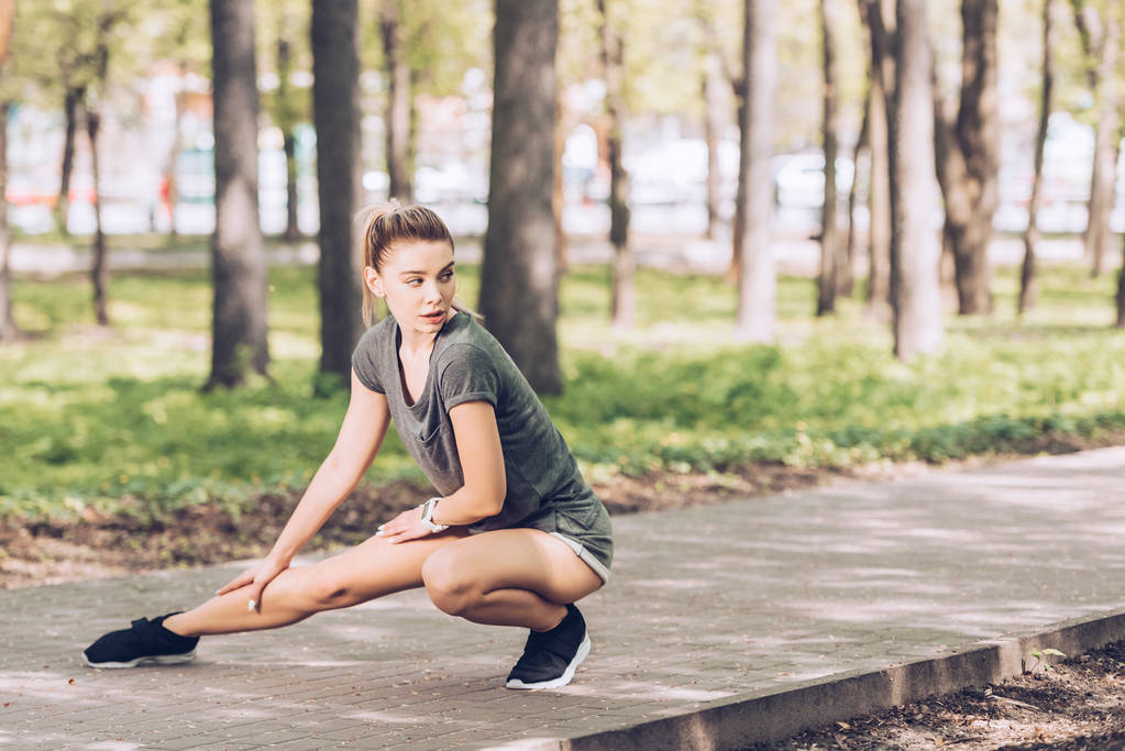 attractive young woman in sportswear looking away while exercising in sunny park - Photo, Image