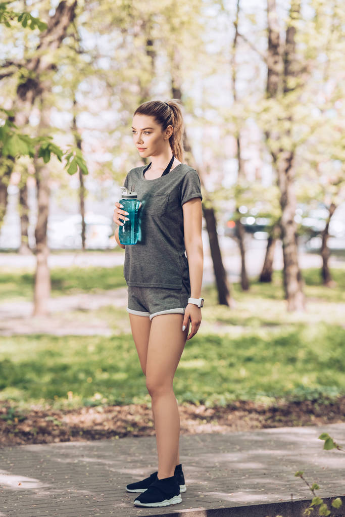 mulher bonita em sportswear segurando garrafa esporte e olhando para longe no parque
 - Foto, Imagem