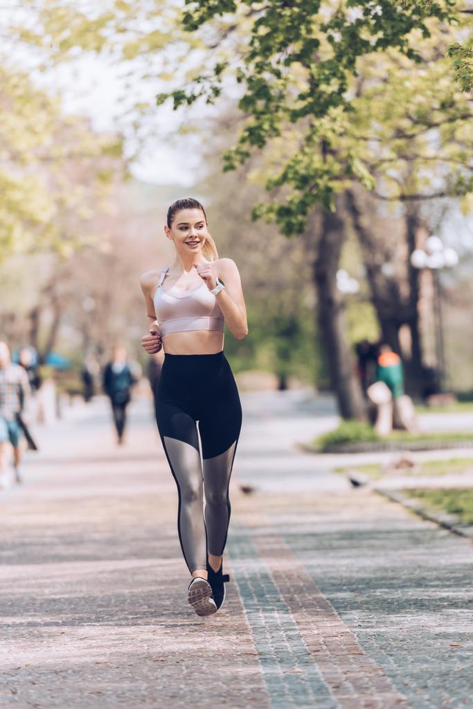 aika urheilija hymyilee lenkillä pitkin leveää kävelytietä puistossa
 - Valokuva, kuva