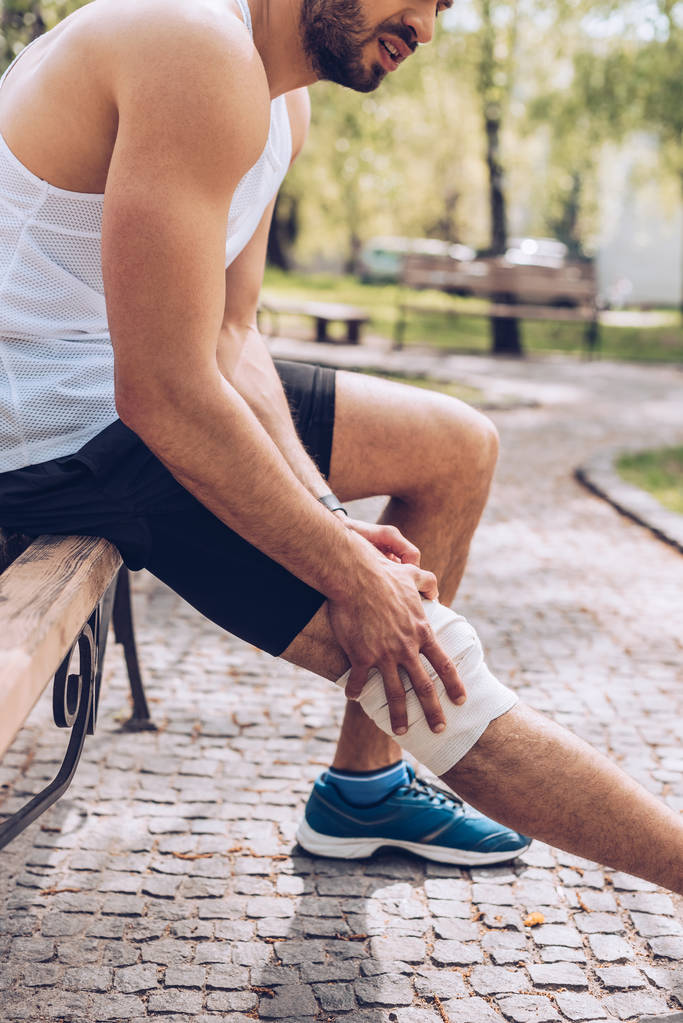 plan recadré d'un sportif assis sur un banc et touchant un bandage élastique sur une jambe blessée
 - Photo, image