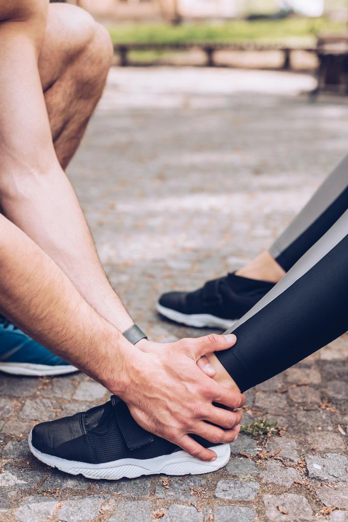 spor ayakkabılı sporcunun yaralı bacağına dokunan sporcunun kısmi görünümü - Fotoğraf, Görsel