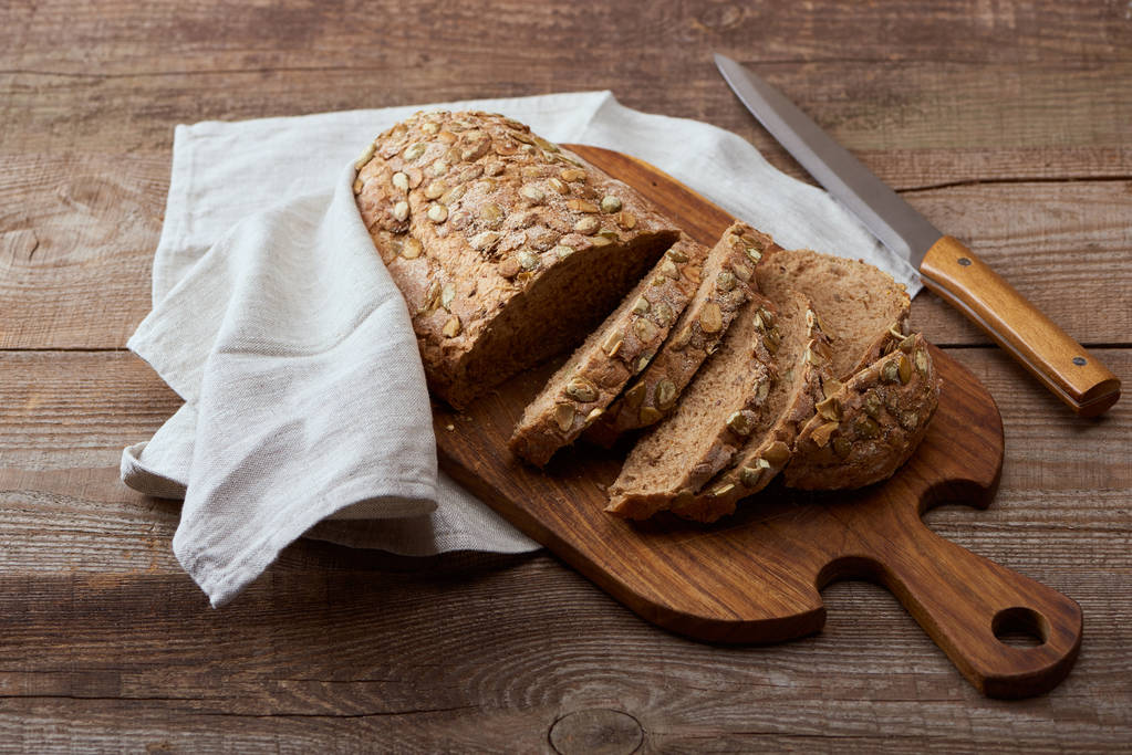 świeży chleb cięte chleba na deski do krojenia w pobliżu białej serwetki i nóż na drewnianym stole - Zdjęcie, obraz
