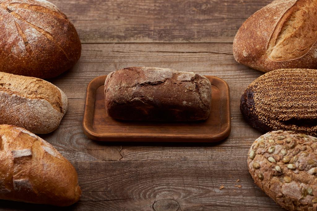 delicious loaves of bread around brown bread on board on wooden table - Photo, Image