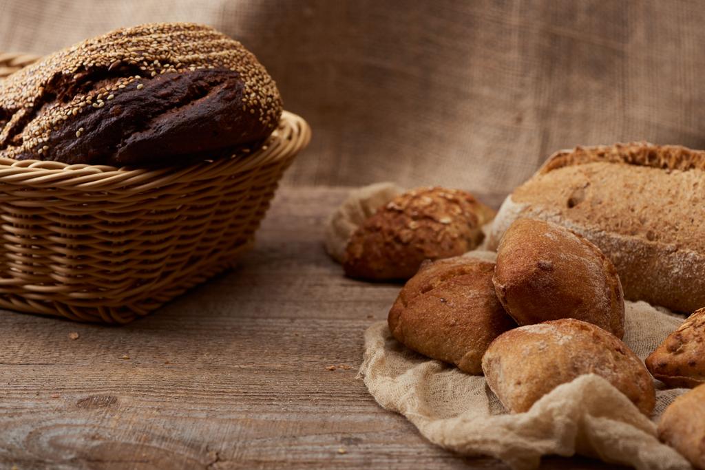 вкусные свежие булочки и хлеб в плетеной коробке на деревянном деревенском столе с тканью
  - Фото, изображение