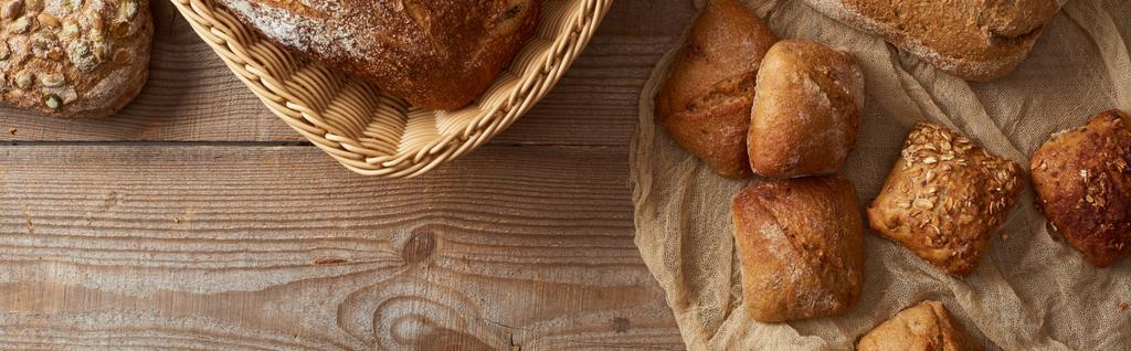 木製のテーブルの上の布の上にウィッカーバスケットとパンで焼きたてのパンのトップビュー、パノラマショット - 写真・画像