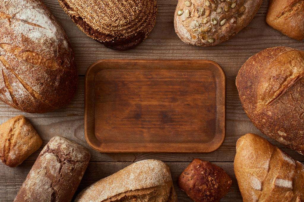pohled na čerstvé domácí bochníky chleba kolem dřevěné prázdné sekací desky - Fotografie, Obrázek