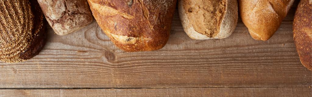 pohled na čerstvé domácí bochníky chleba na dřevěném stole, panoramatický záběr - Fotografie, Obrázek