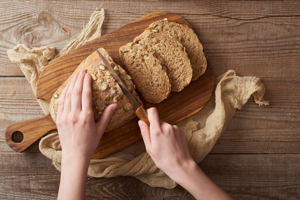 сверху вид женщины, режущей хлеб с семенами на деревянной доске
 - Фото, изображение