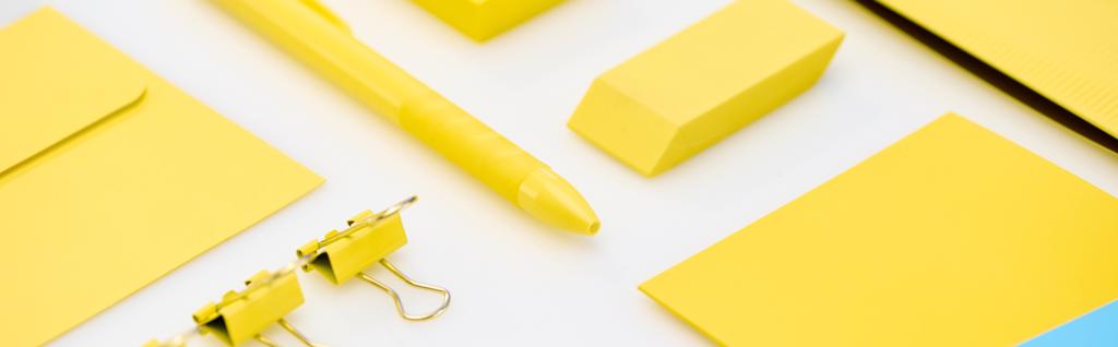 panoramatický záběr žlutého pera, papírových sponek, gumy, štítků a obálek na bílém pozadí - Fotografie, Obrázek