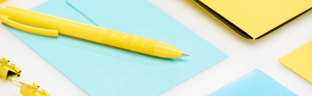 Panoramaaufnahme von gelbem Ordner, Büroklammern und Stift auf blauem Umschlag auf weißem Hintergrund - Foto, Bild