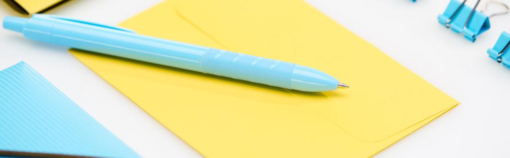 panoramatický záběr modré složky, papírové sponky a pero na žluté obálce na bílém pozadí - Fotografie, Obrázek