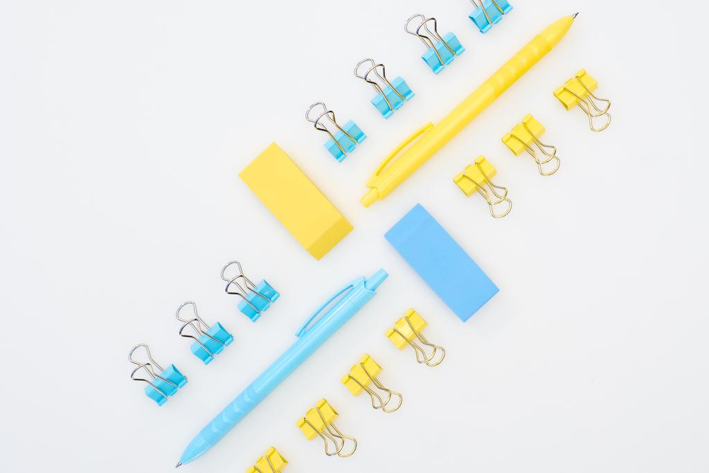 platte lay van gele en blauwe gommen, pennen en paperclips geïsoleerd op wit - Foto, afbeelding