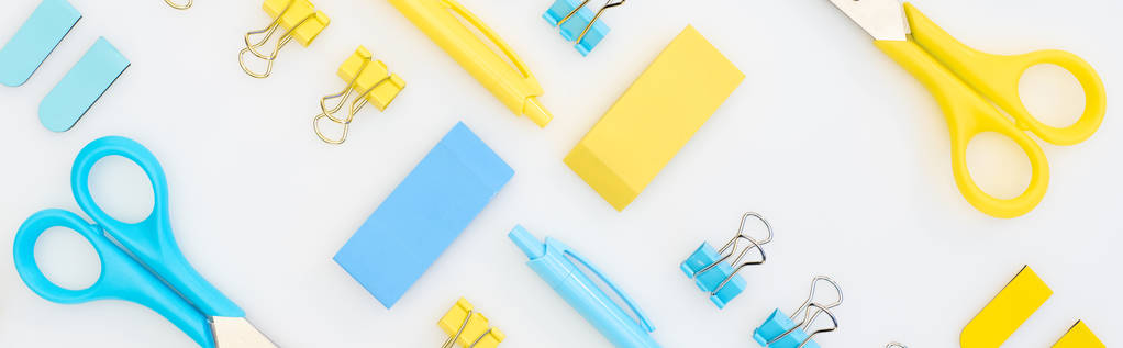 panoramische shot van gele en blauwe gommen, pennen, scharen en paperclips geïsoleerd op wit - Foto, afbeelding
