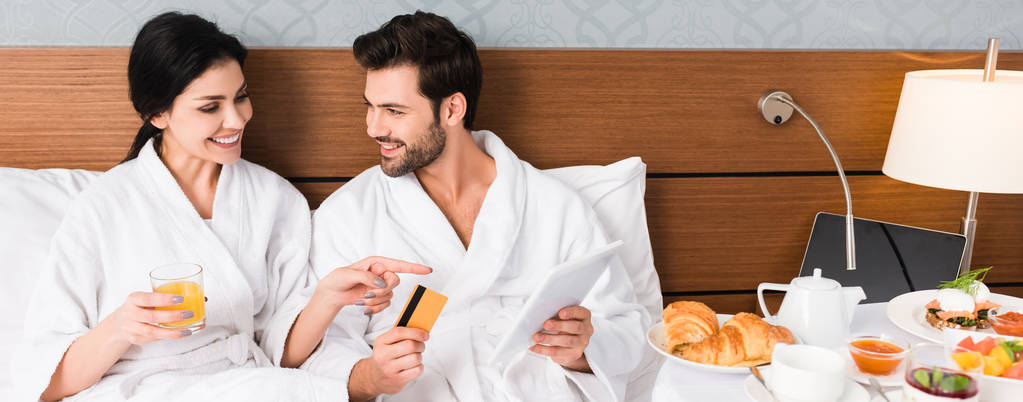panoráma szemcsésedik-ból boldog asszony mutatva-val ujj-on reggeli mellett ember-val hitelkártya és digitális tabletta  - Fotó, kép