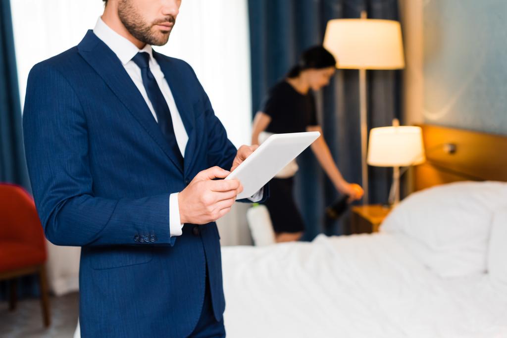 περικομμένη όψη του ανθρώπου χρησιμοποιώντας ψηφιακό δισκίο κοντά υπηρέτρια στο δωμάτιο του ξενοδοχείου  - Φωτογραφία, εικόνα