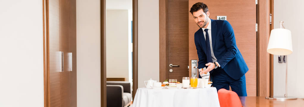 Panoramaaufnahme einer gut gelaunten Empfangsdame in formeller Kleidung, die beim Frühstück im Hotelzimmer gestikuliert  - Foto, Bild