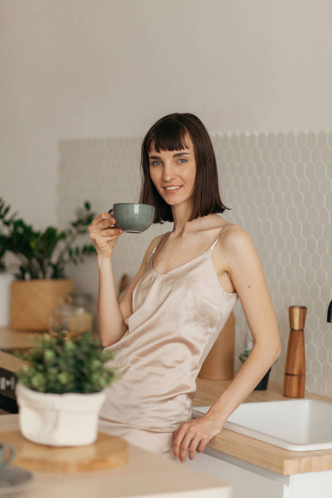 Una ragazza con un sorriso in pigiama in cucina. Incontra la mattina di sole. Prepara delizioso caffè
. - Foto, immagini