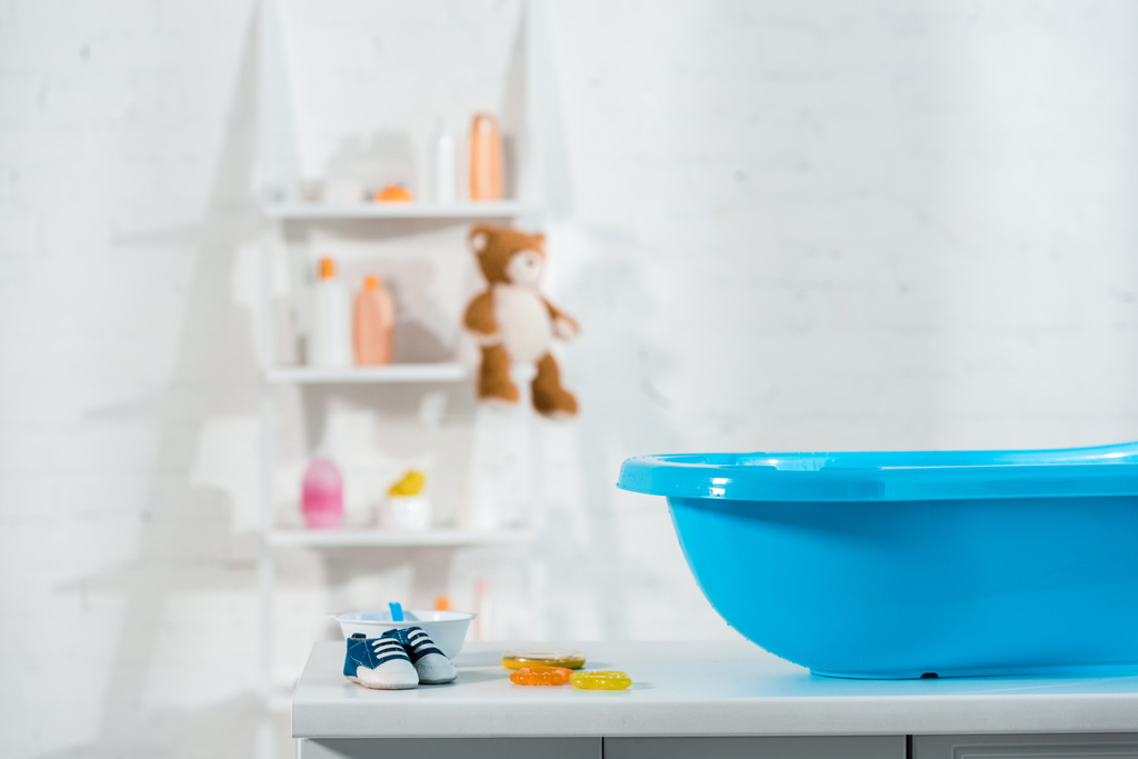 banheira de bebê azul perto de tênis de bebê e brinquedos no banheiro
  - Foto, Imagem