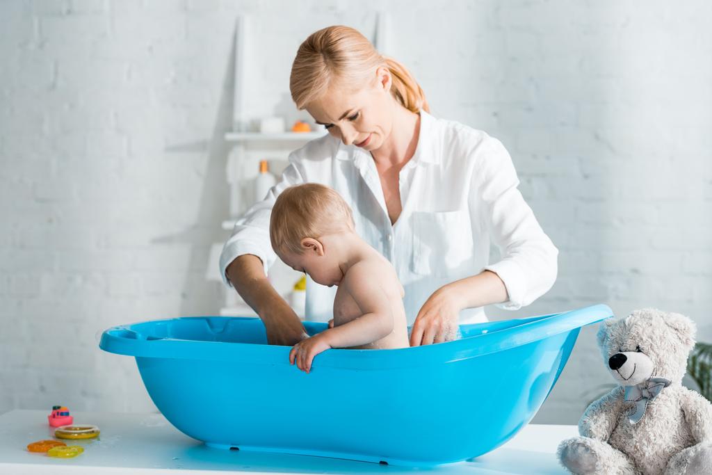 красива мати, що стоїть біля малюка у дитячій ванні
  - Фото, зображення