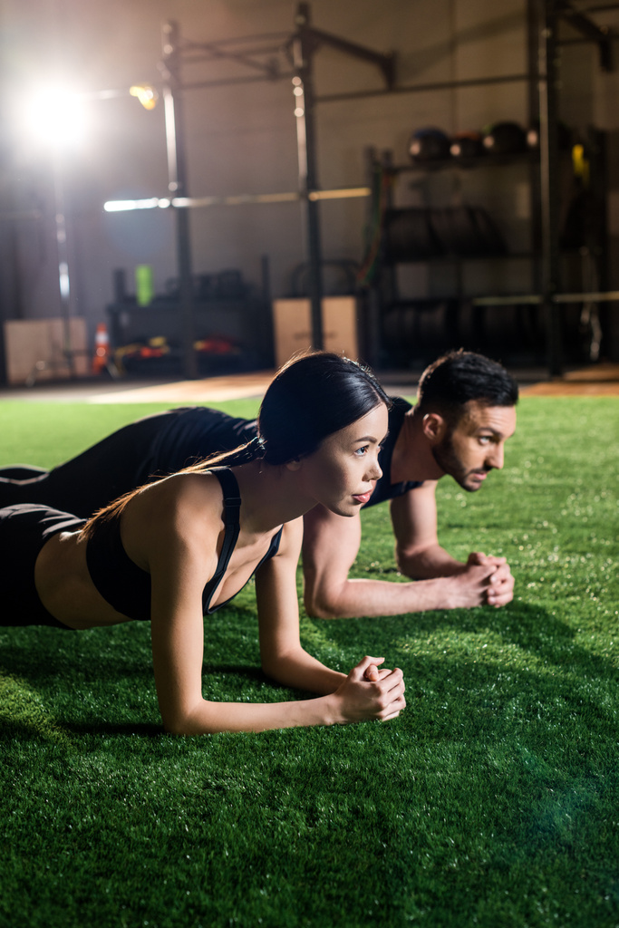 selective focus of attractive woman and bearded man doing plank exercise on green grass  - Photo, Image