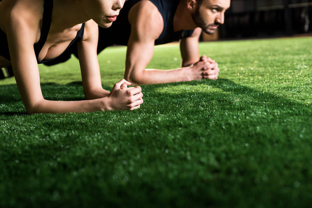 cropped view of woman doing plank exercise with handsome man on grass - Photo, Image
