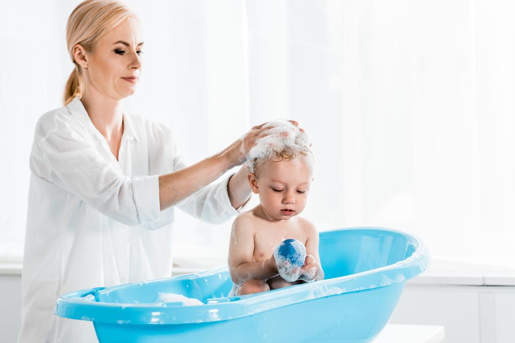 atraktivní matka mytí hlavy roztomilým batole v koupelně  - Fotografie, Obrázek