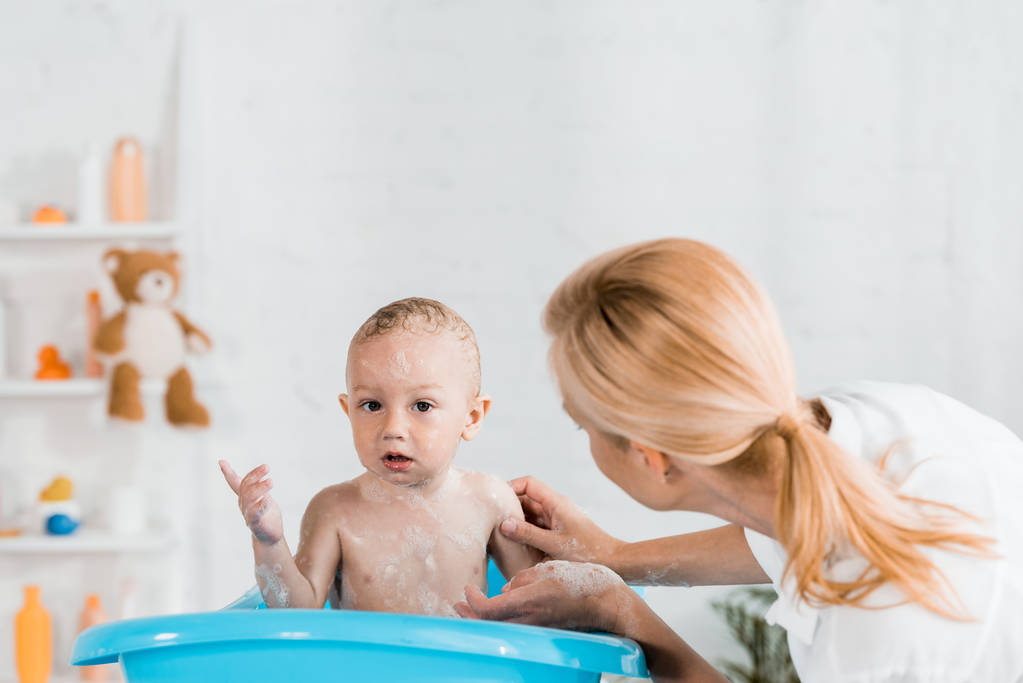  Blondine Mutter schaut Kleinkind-Sohn mit Finger im Badezimmer an  - Foto, Bild