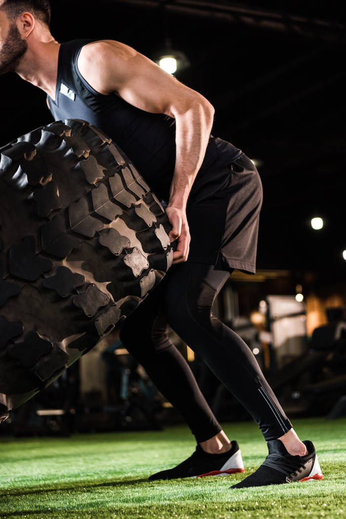 cropped view of athletic man working out with car tire on green grass  - Photo, Image