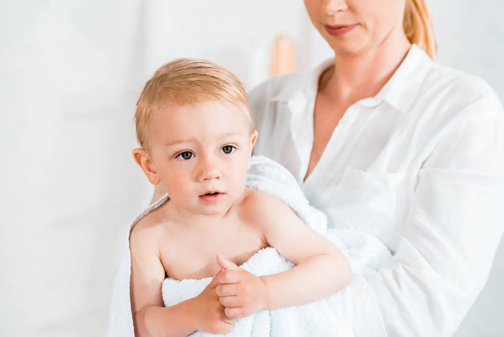 bijgesneden weergave van blonde moederholding in Arms schattig peuter zoon in badkamer  - Foto, afbeelding