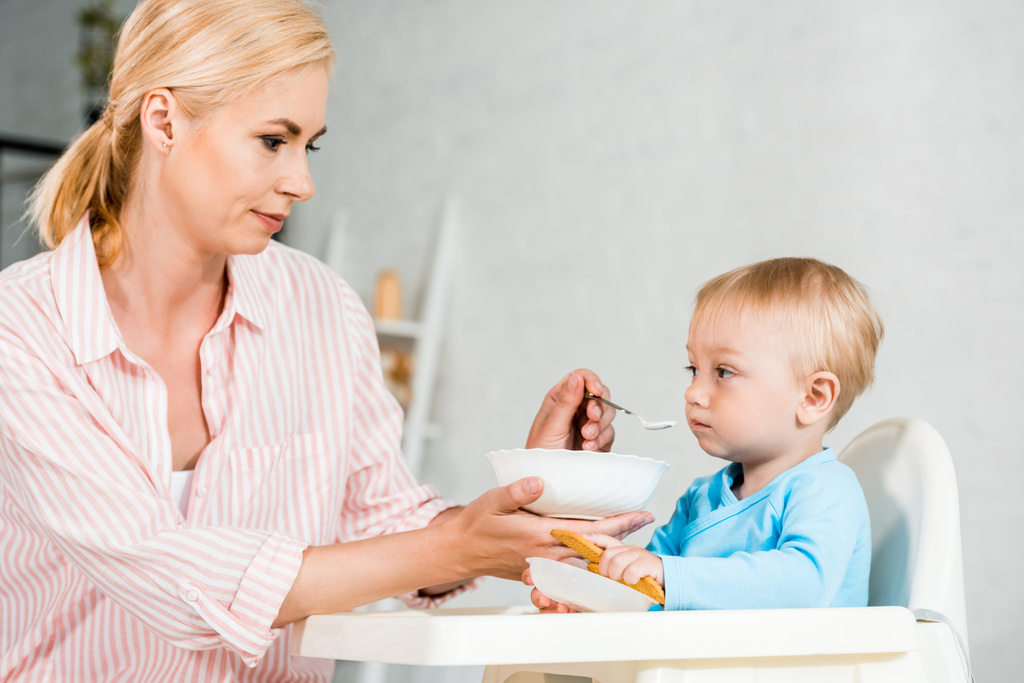 blond matka trzymanie i karmienie słodkie dziecko w domu  - Zdjęcie, obraz