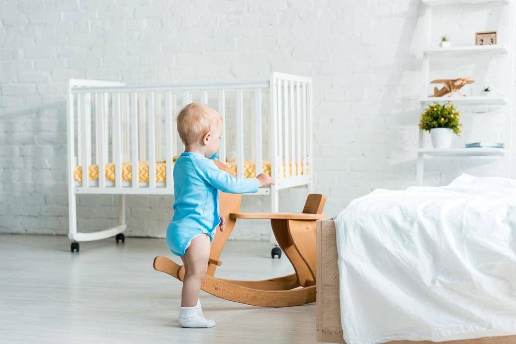 söpö lapsi lapsi seisoo lähellä puinen keinuhevonen modernissa makuuhuoneessa
  - Valokuva, kuva