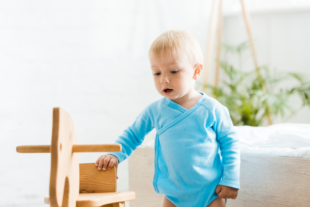 toddler kid standing near wooden rocking horse in bedroom  - Photo, Image