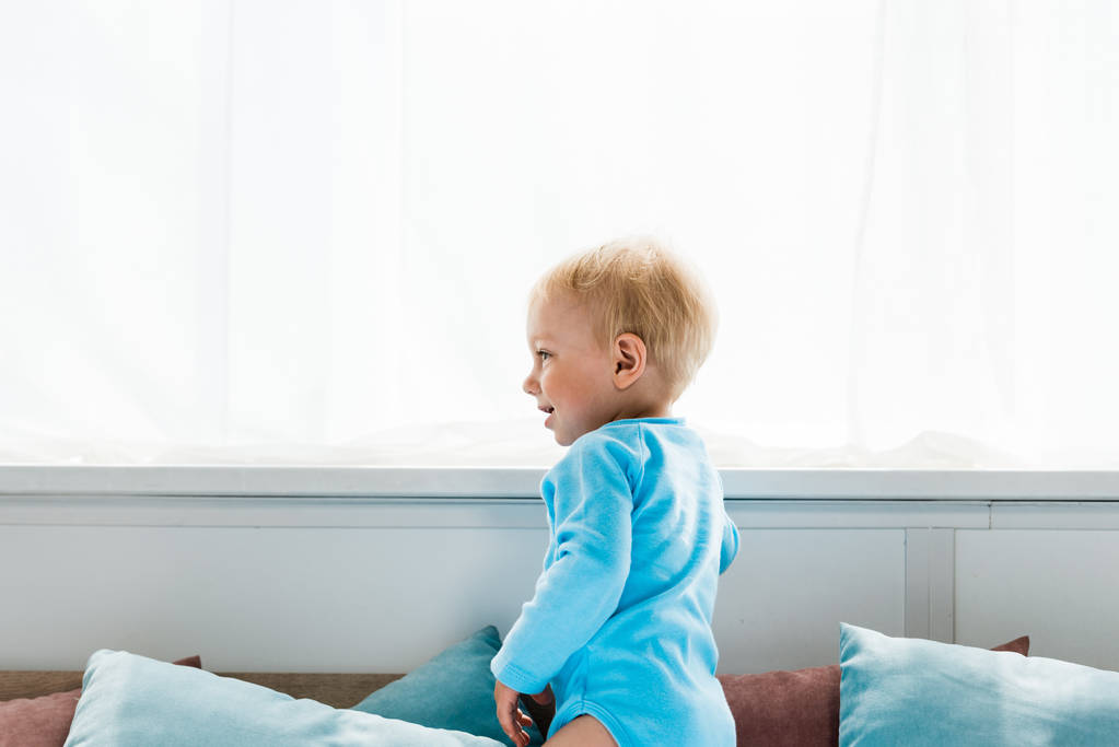 fröhliches Kleinkind stehend und lächelnd im Schlafzimmer  - Foto, Bild