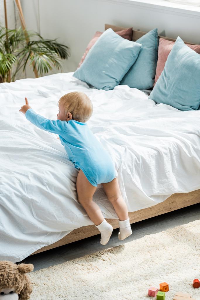 tout-petit enfant rampant sur le lit avec literie blanche et pointant du doigt à la maison
  - Photo, image