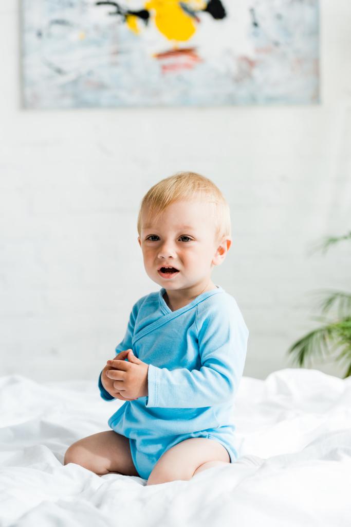 lindo niño sentado en la cama con ropa de cama blanca en casa
  - Foto, Imagen