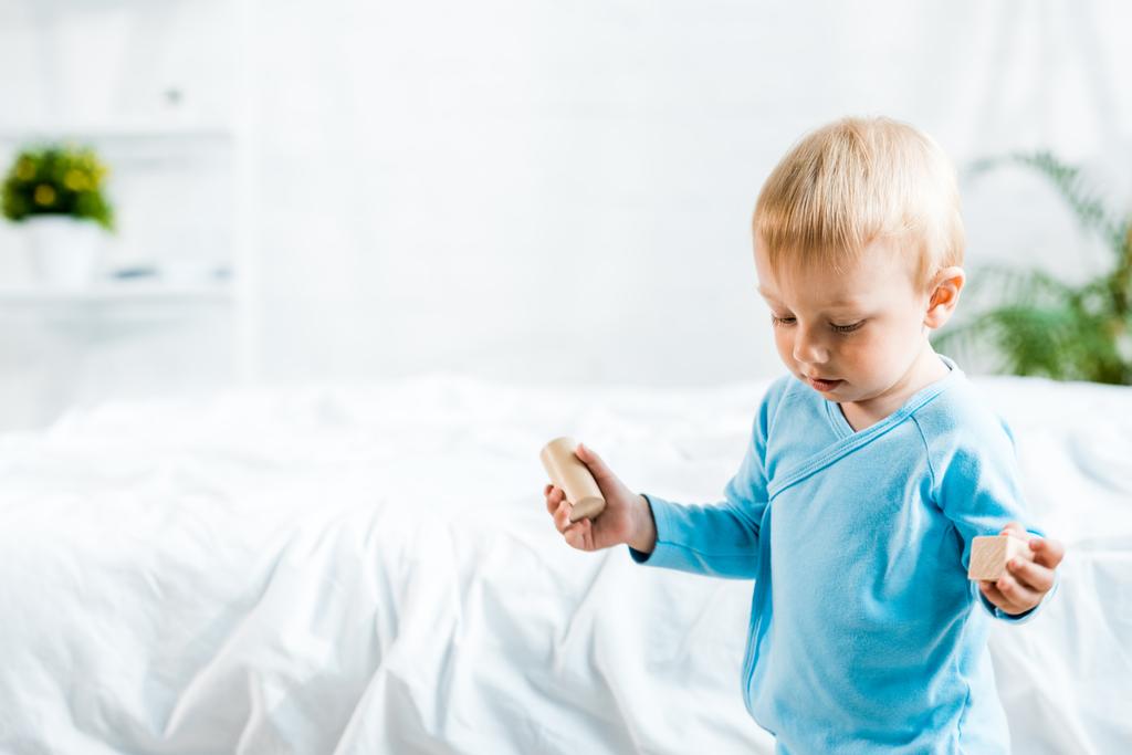adorable tout-petit enfant debout avec des jouets en bois près du lit à la maison
 - Photo, image