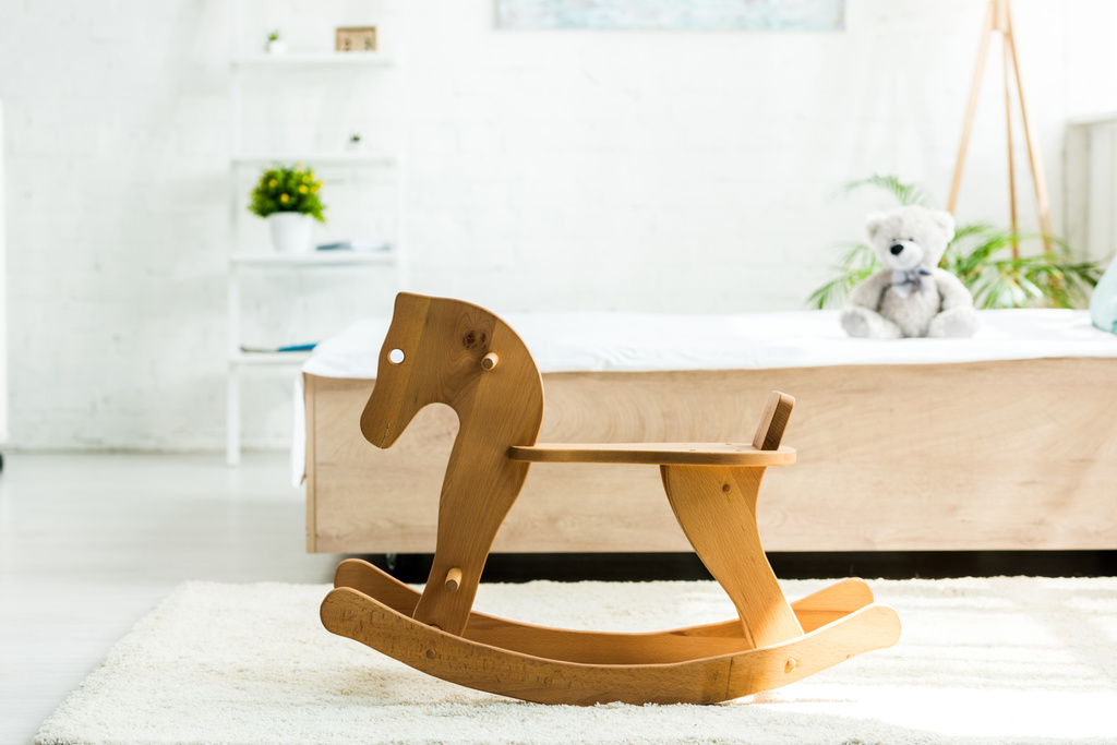 selectieve focus van houten schommelpaard in de buurt van bed met wit beddengoed en teddybeer - Foto, afbeelding