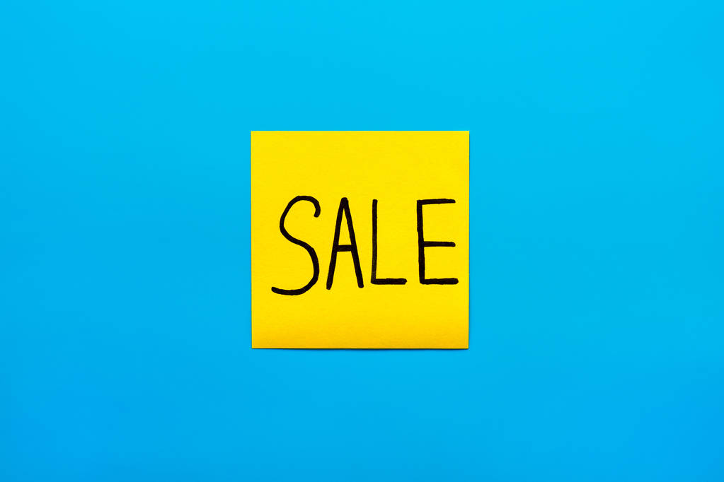 Kereskedelmi, marketing, emlékeztető és kombinált koncepció-közelről fekete kézzel írt felirat eladó szó egy sárga négyzet alakú matrica kék háttér másolás spase, vízszintes tájolású - Fotó, kép