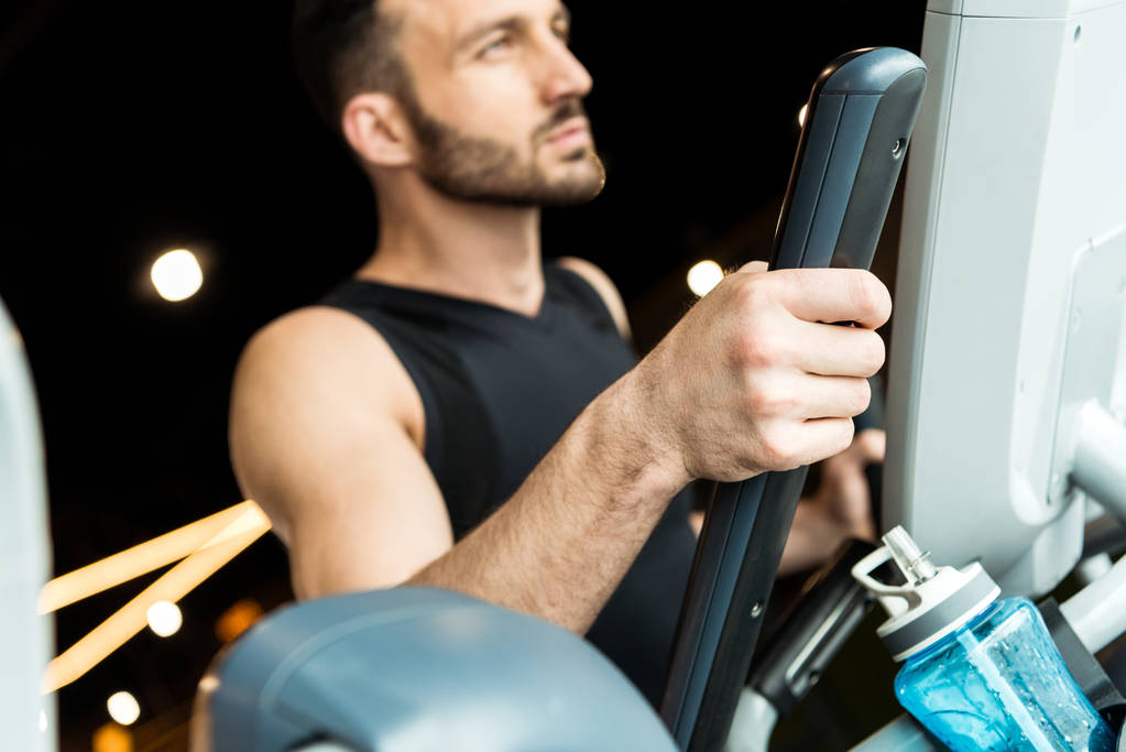 selective focus of sport bottle near handsome athletic man working out on exercise bike  - Photo, Image
