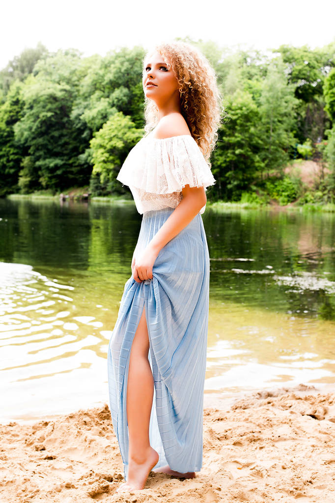 Kudrnatá žena ve stylových šatech na písčitém břehu jezera  - Fotografie, Obrázek