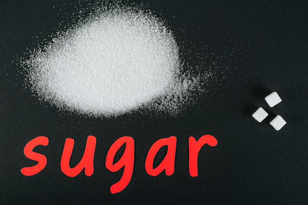 ylhäältä näkymä valkoinen sokeri kiteet ja kuutiot lähellä punainen paperi leikkaa sana sokeri mustalla pohjalla
 - Valokuva, kuva