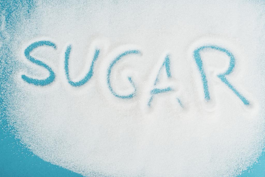 верхний вид слова сахар, сделанный на брызганых кристаллах белого сахара на голубой поверхности
 - Фото, изображение