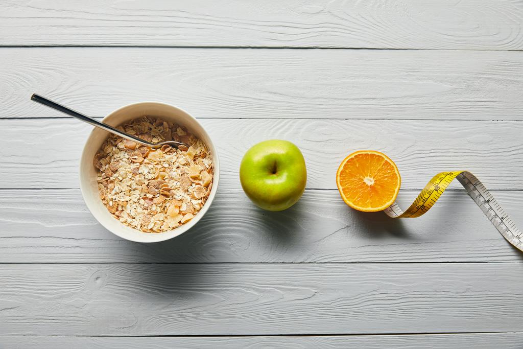 plat étendu avec céréales pour petit déjeuner dans un bol, pomme, orange et ruban à mesurer sur fond blanc en bois
 - Photo, image