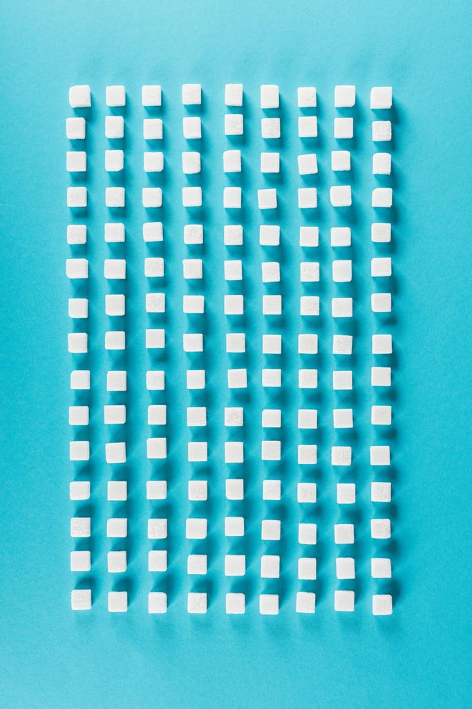 vista superior de cubos de açúcar branco dispostos em linhas na superfície azul
 - Foto, Imagem