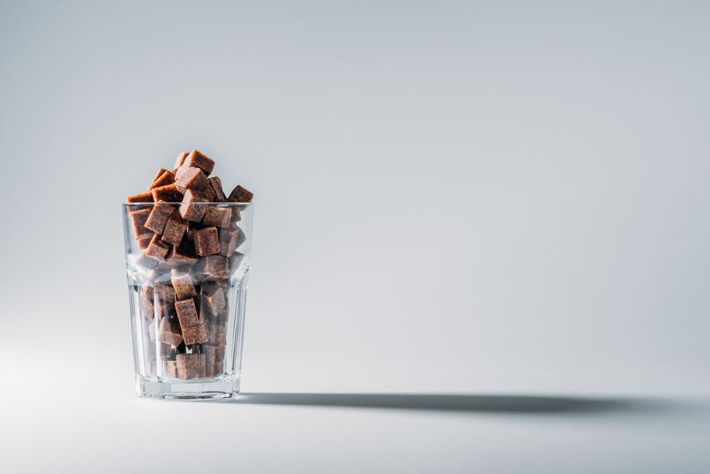 kopya alanı ile gri arka plan üzerinde kahverengi şeker küpleri dolu cam - Fotoğraf, Görsel