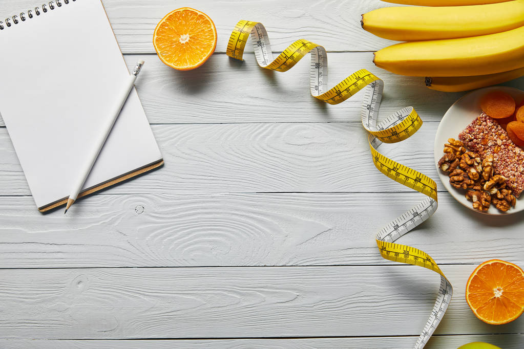 Draufsicht auf Maßband, Diätfutter und leeres Notizbuch auf weißem Holzgrund mit Kopierraum - Foto, Bild